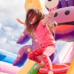 Why renting an inflatable for your event is a great idea. A young girl joyfully leaps on an inflatable slide, her hair flowing in the air as she enjoys the playful activity.