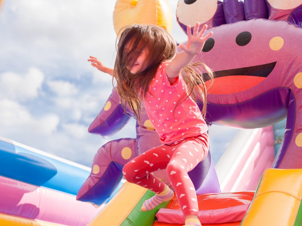 Why renting an inflatable for your event is a great idea. A young girl joyfully leaps on an inflatable slide, her hair flowing in the air as she enjoys the playful activity.