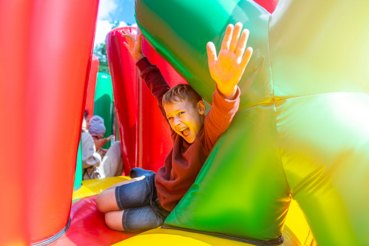 Prime bouncy castles for rent. A young boy joyfully jumps on an inflatable bouncer, filled with vibrant colors and surrounded by a playful atmosphere.
